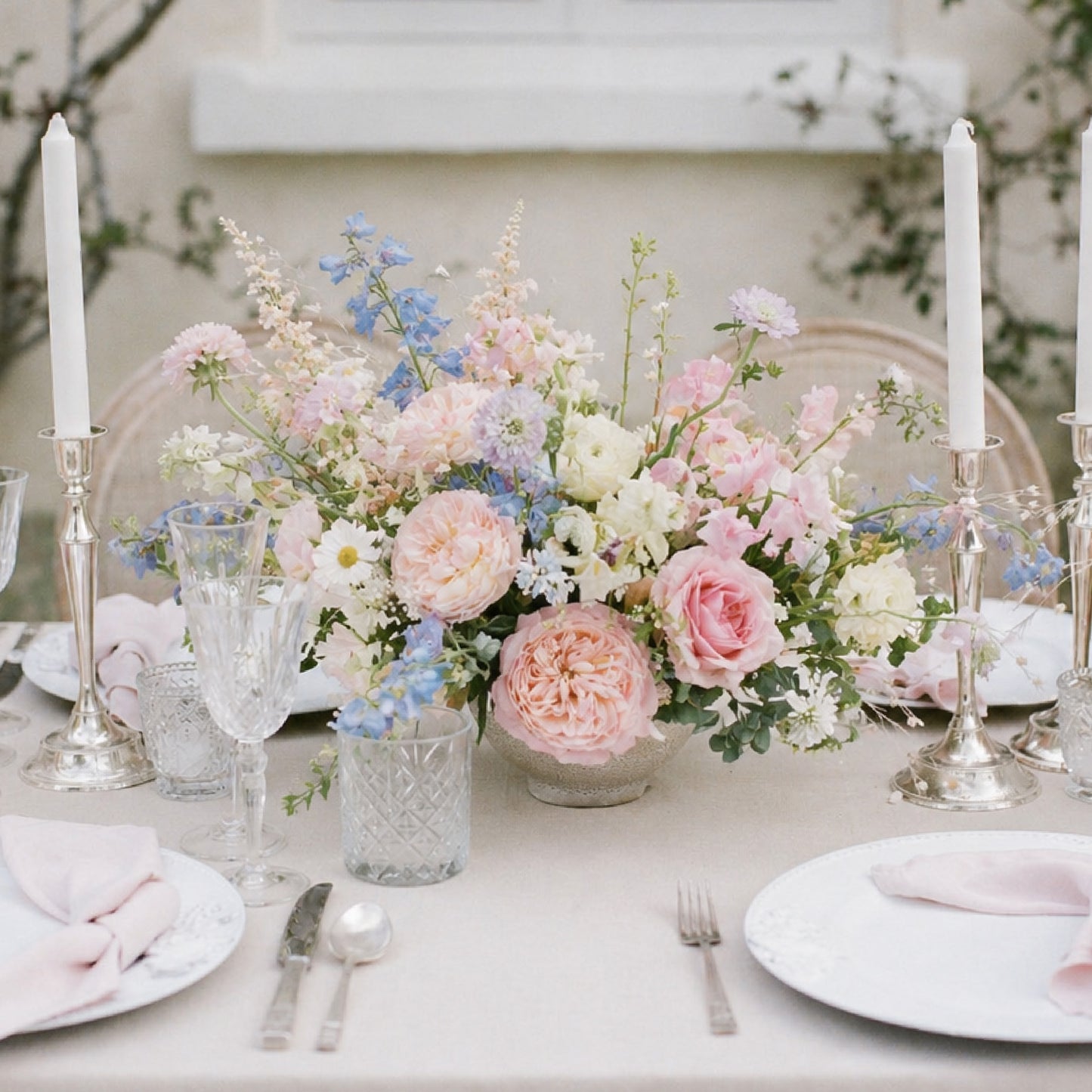 Pastel still-life wedding centerpiece with blush, lavender, blue, cream, and white garden flowers