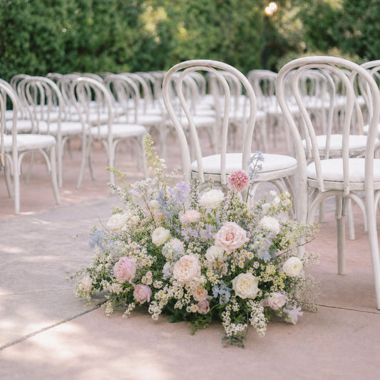 Pastel meadow arrangement styled beside outdoor wedding ceremony aisle seating.