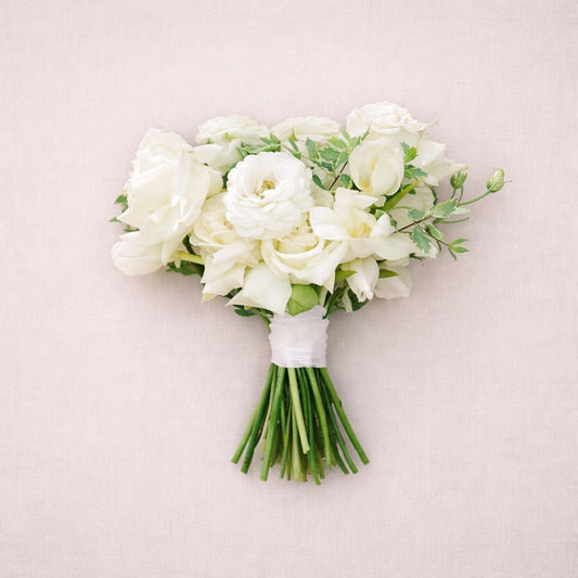 Porcelain bridesmaid bouquet featuring white roses and delicate seasonal blooms styled against soft neutral backdrop.