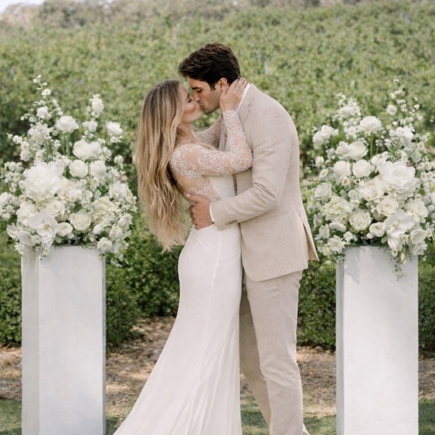 Porcelain meadow arrangement pair with airy white floral compositions framing an outdoor ceremony setting beside bride and groom.
