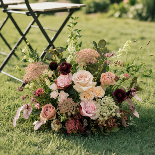 Moody burgundy and blush meadow arrangements styled along outdoor wedding aisle detail