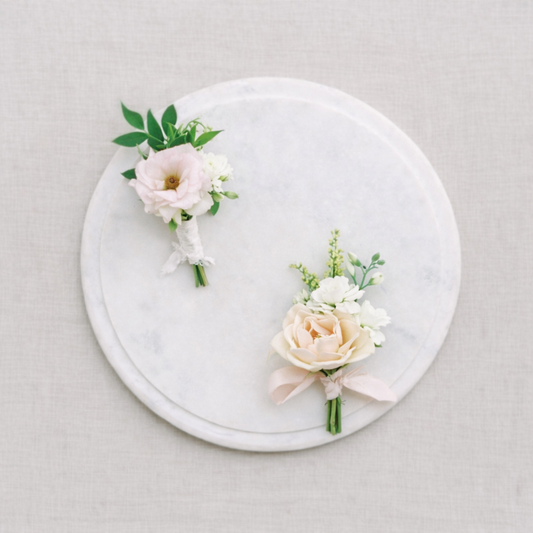 Rosewater boutonnières with soft blush and ivory blooms styled on marble tray.