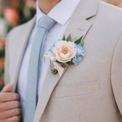 Pastel wedding boutonnière with blush rose and powder blue flowers on beige suit.