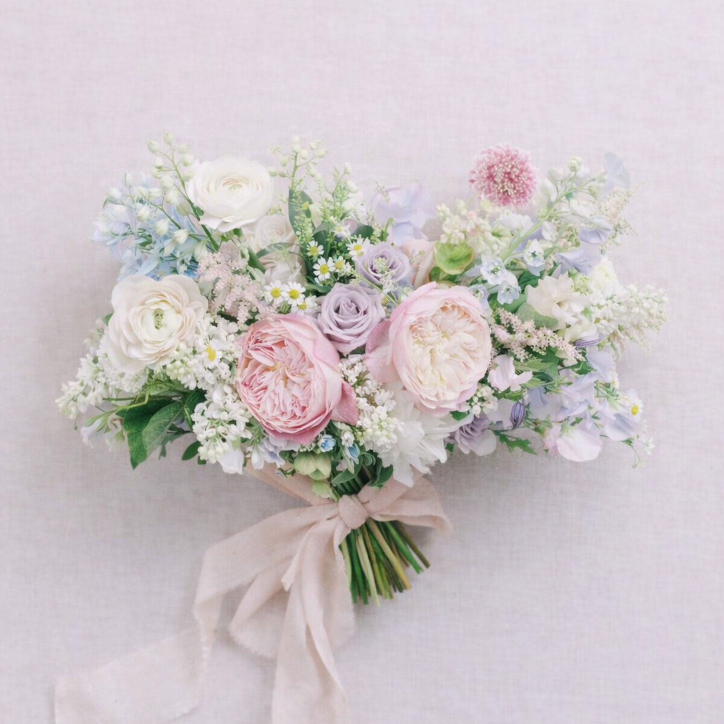 Close-up of pastel bridal bouquet with blush roses, lavender blooms, and airy seasonal flowers.