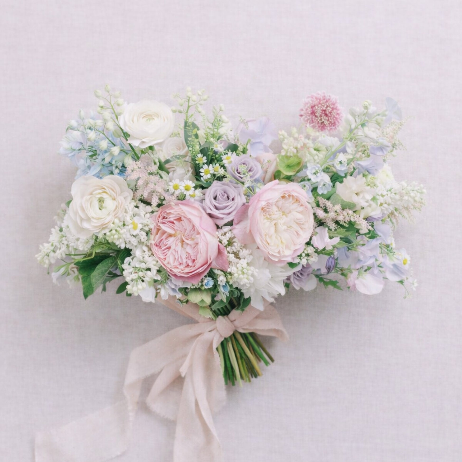 Close-up of pastel bridal bouquet with blush roses, lavender blooms, and airy seasonal flowers.