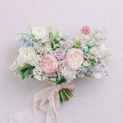 Close-up of pastel bridal bouquet with blush roses, lavender blooms, and airy seasonal flowers.