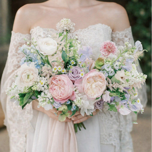 Pastel bridal bouquet with blush, lavender, blue, cream, and white garden flowers.
