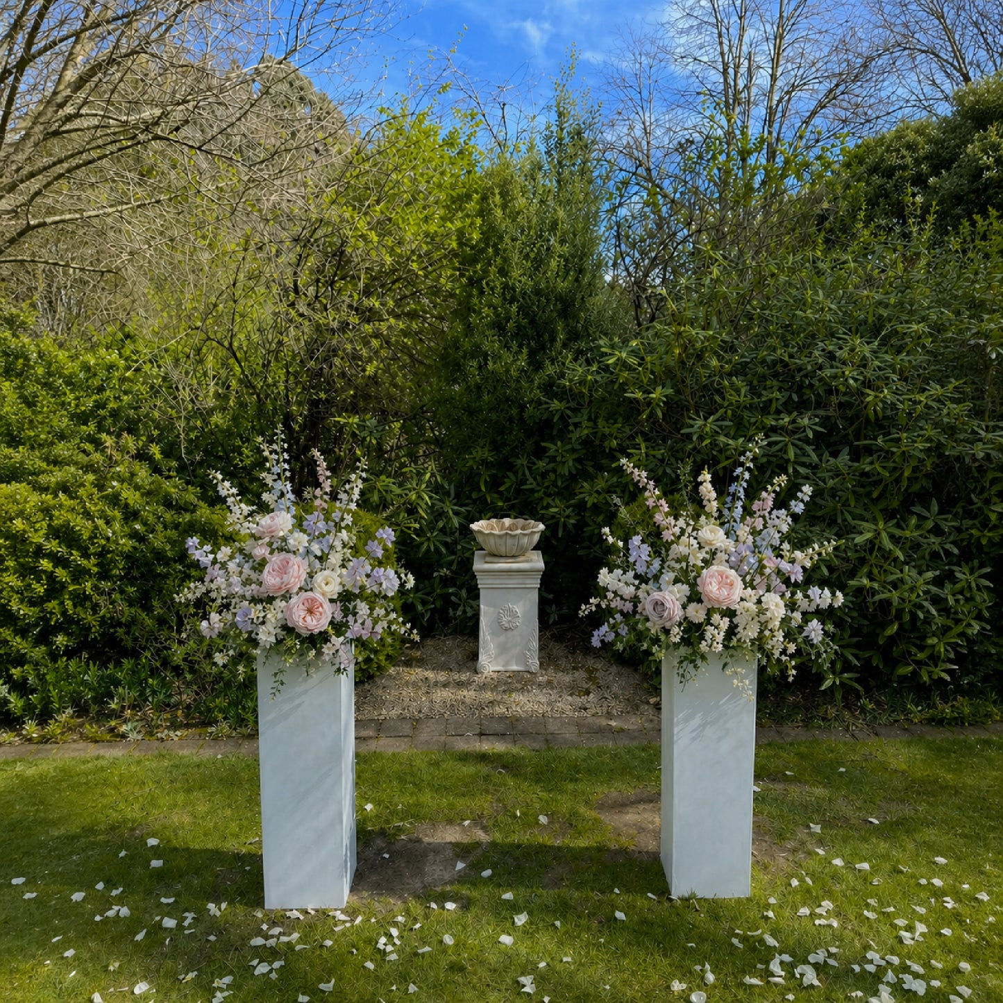 Pastel meadow ceremony arrangements displayed on pedestals with blush, lavender, blue, and ivory flowers.