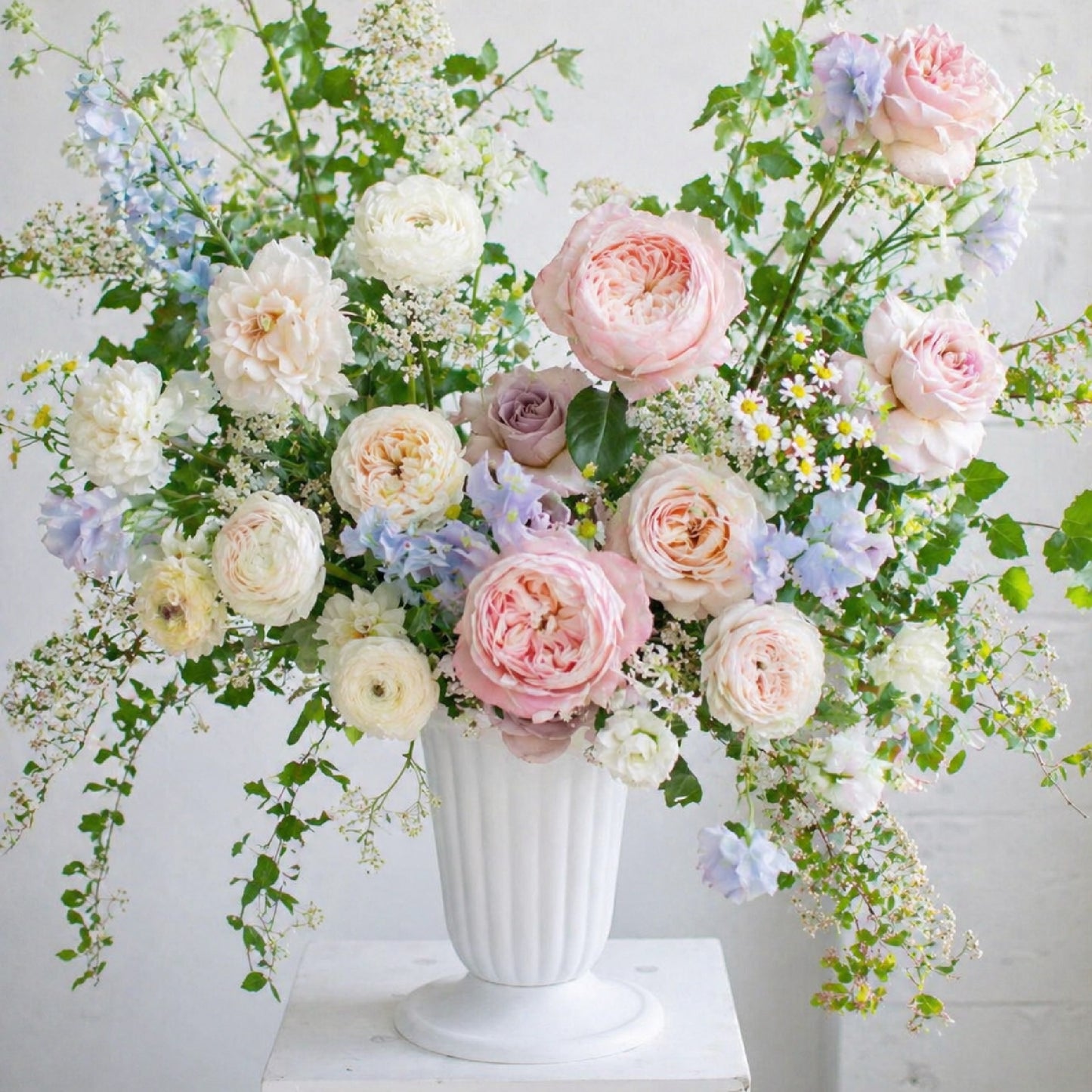 Close-up of pastel ceremony urn arrangement with blush, lavender, blue, and ivory garden flowers.