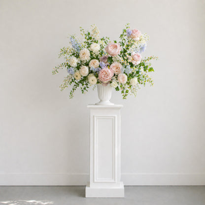 Pastel ceremony urn arrangement displayed on pedestal with blush, blue, lavender, and ivory garden flowers