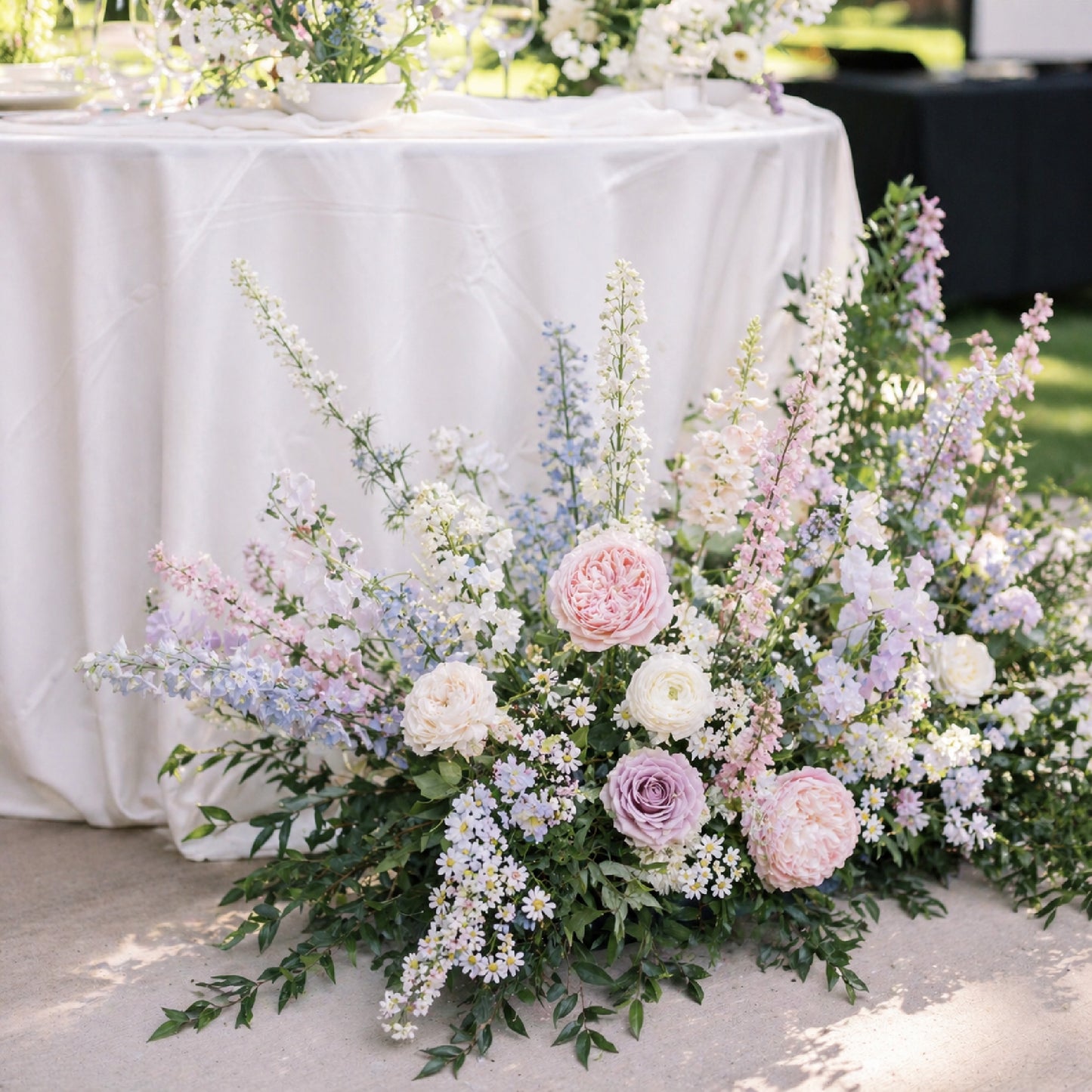 Pastel ground meadow arrangement styled beside romantic wedding cocktail table.