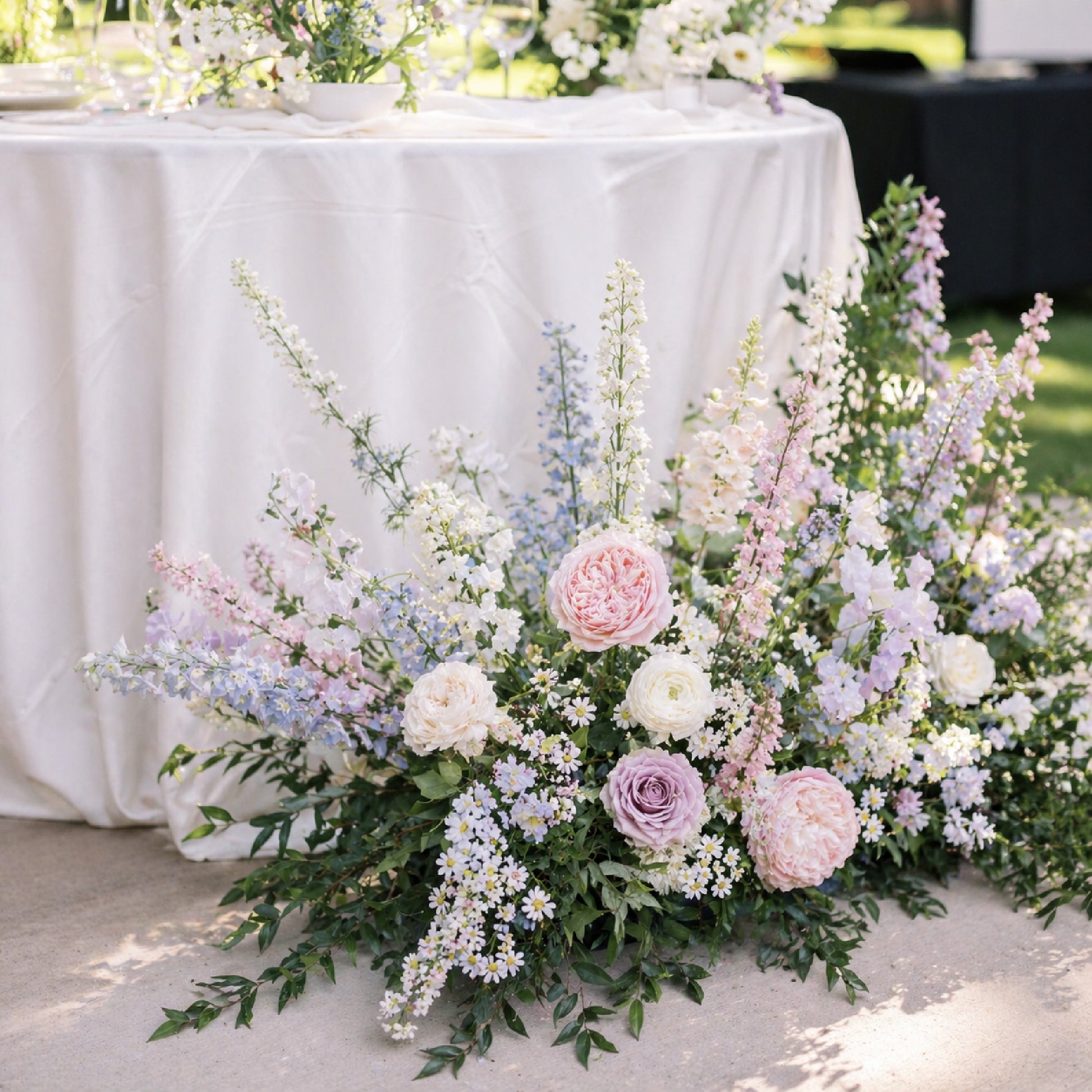 Pastel ground meadow arrangement styled beside romantic wedding cocktail table.