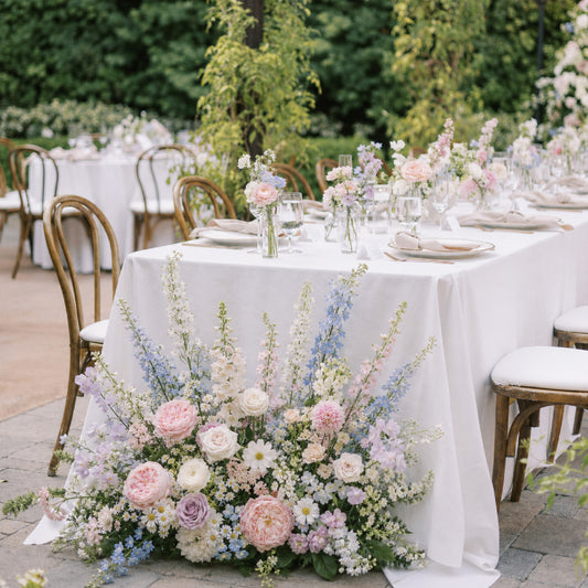 Pastel ground meadow arrangement styled beside romantic outdoor wedding reception table.