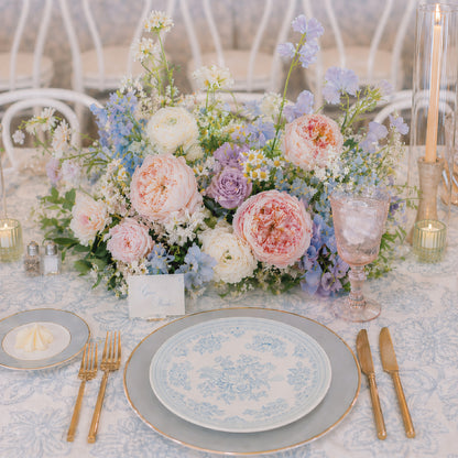 Pastel meadow wedding centerpiece with blush, blue, lavender, cream, and white garden flowers.