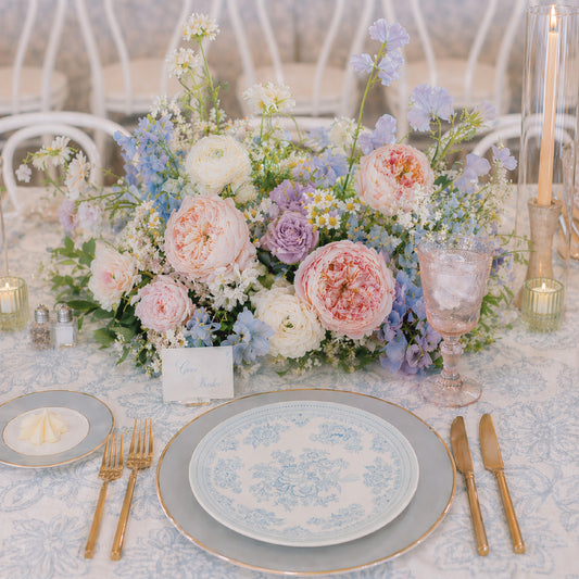 Pastel meadow wedding centerpiece with blush, blue, lavender, cream, and white garden flowers.