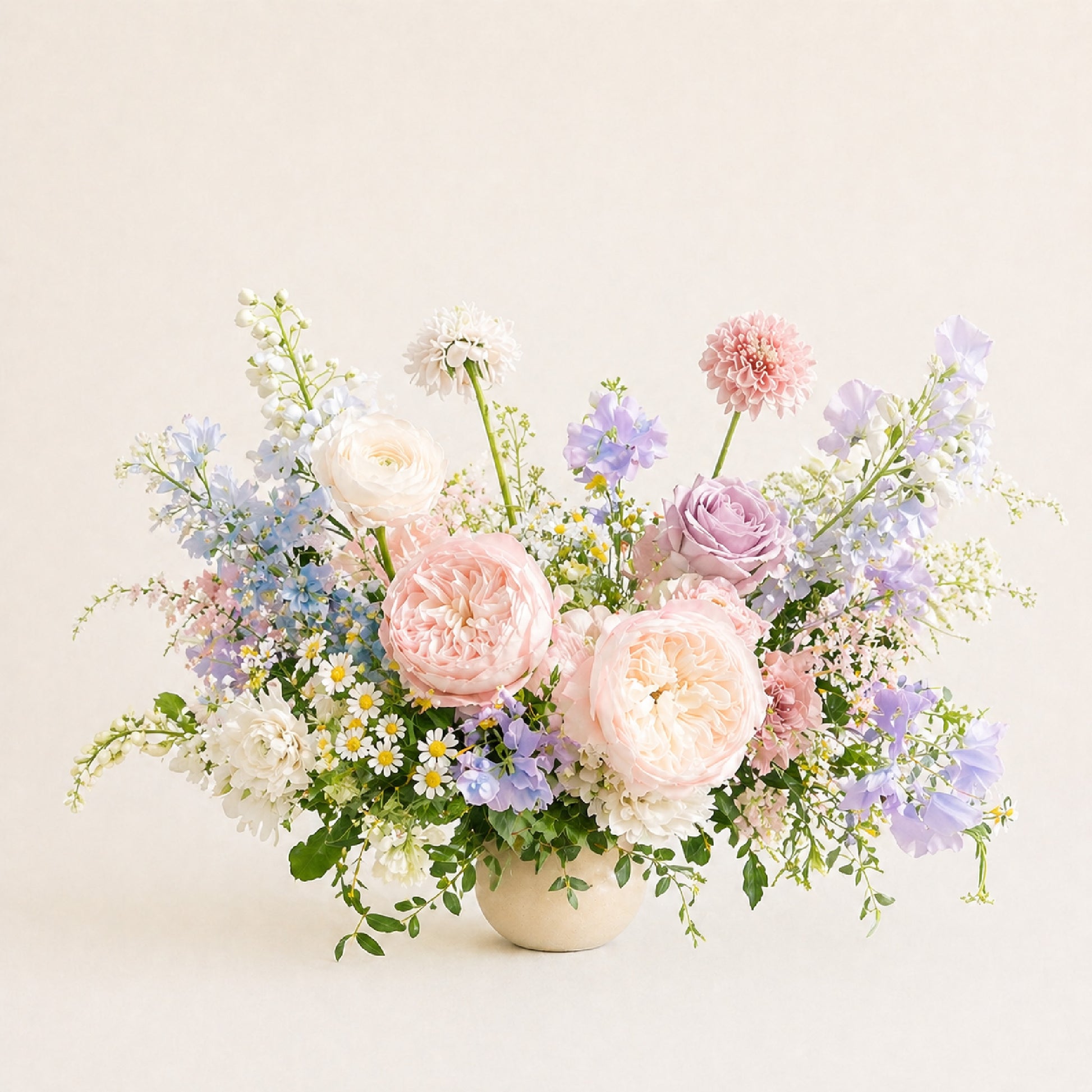 Pastel still-life wedding centerpiece with blush, lavender, blue, and ivory garden flowers in a small ceramic bowl