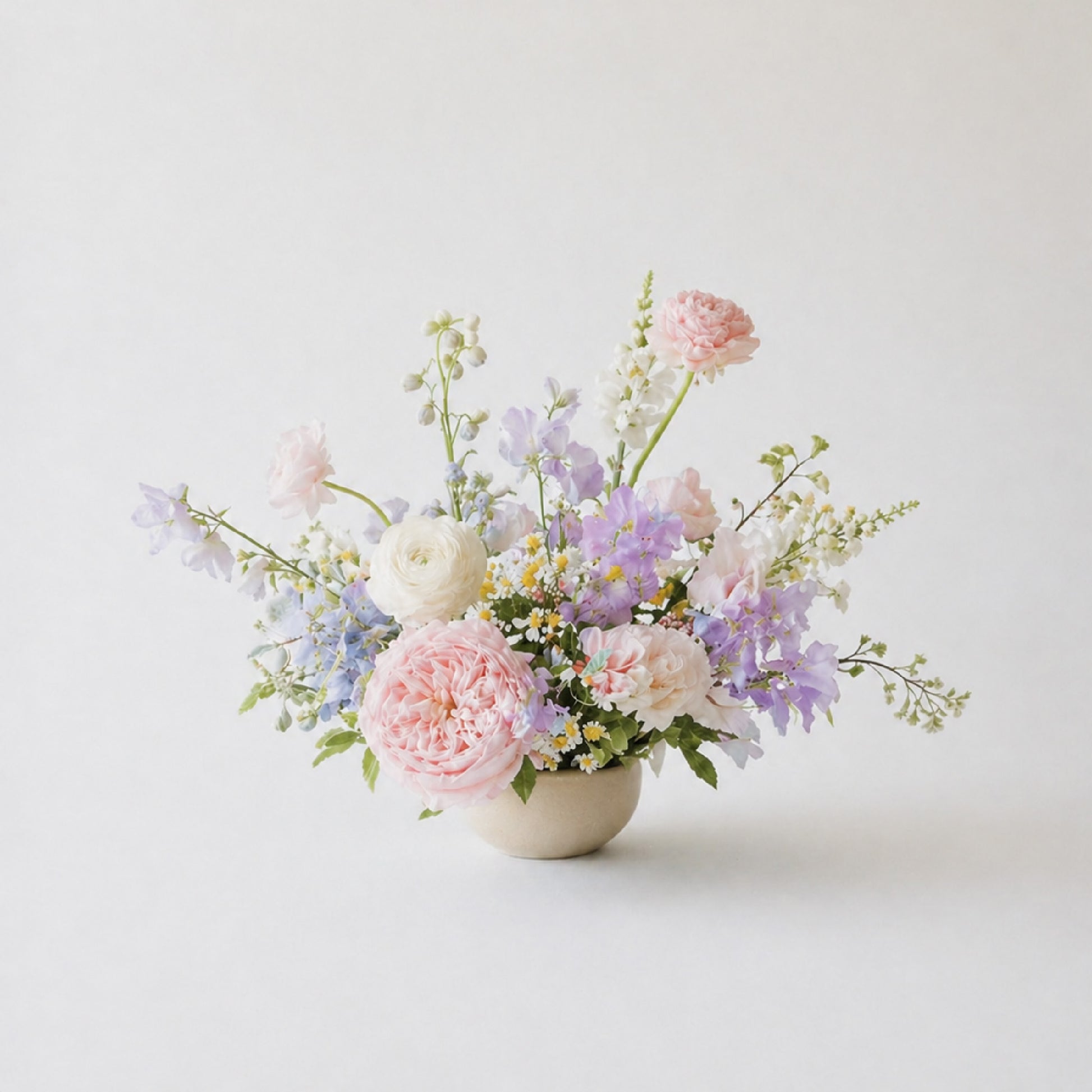 Pastel still-life wedding centerpiece with blush, lavender, blue, and ivory garden flowers