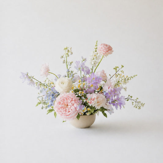 Pastel still-life wedding centerpiece with blush, lavender, blue, and ivory garden flowers