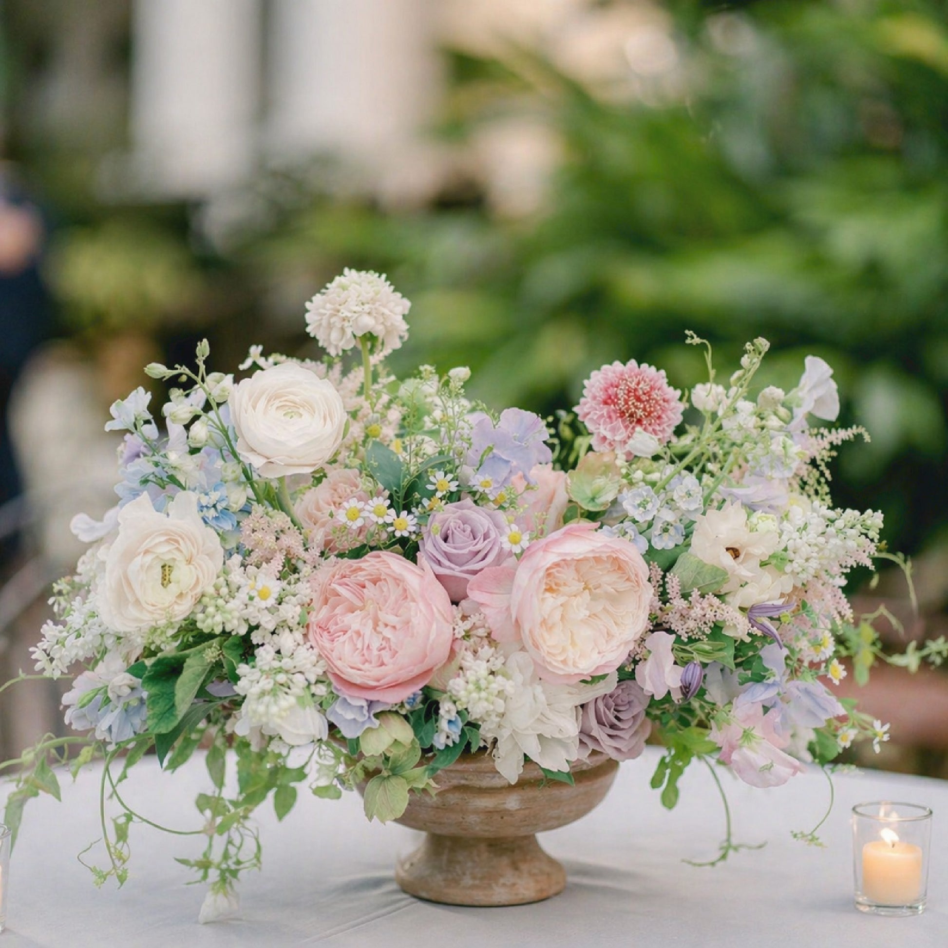Pastel heirloom clay compote wedding centerpiece with blush, lavender, blue, cream, and white garden flowers.