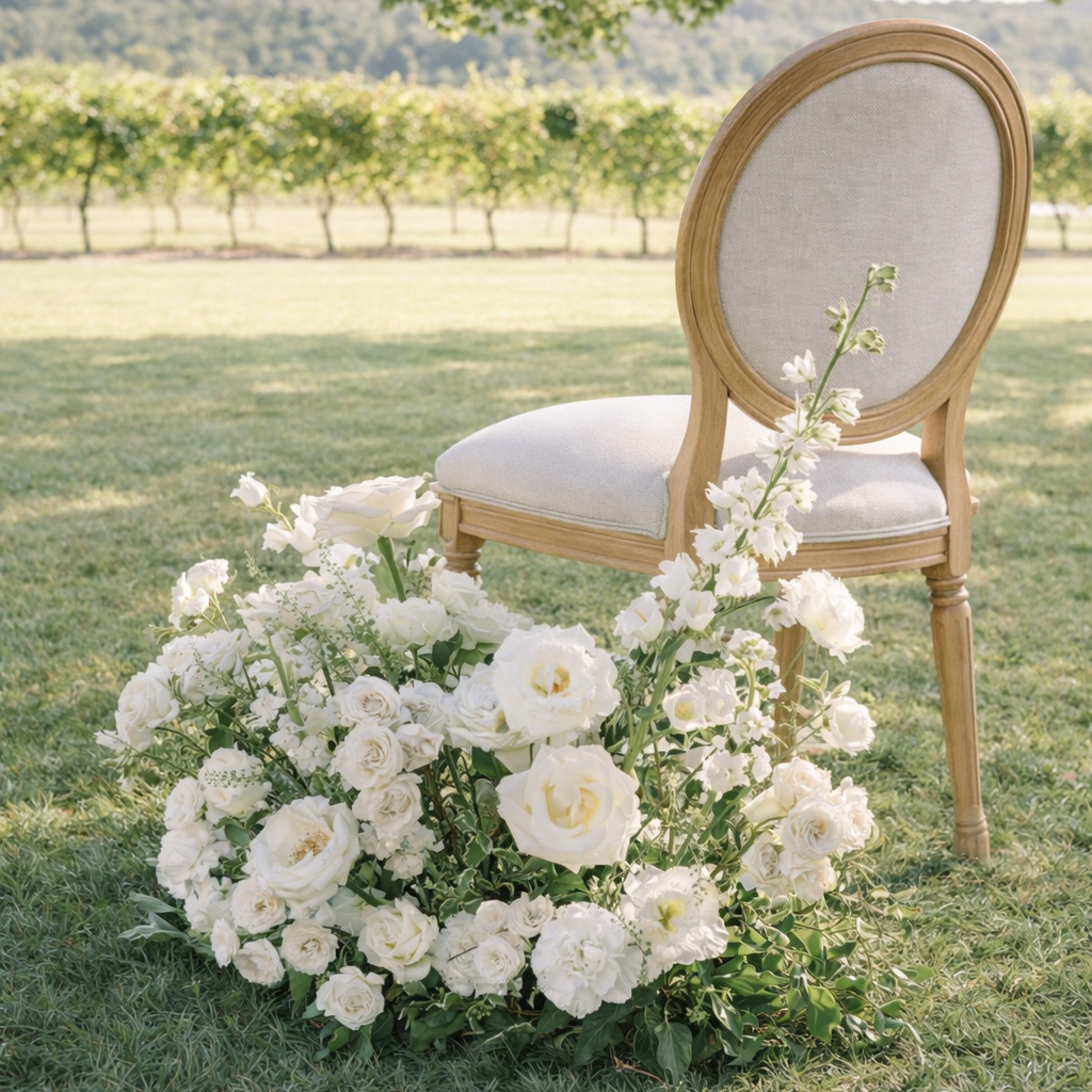 Porcelain Additional Ground Meadow Arrangement with airy white florals styled organically as an aisle marker beside a chair in a nineyard.