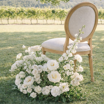Porcelain Additional Ground Meadow Arrangement with airy white florals styled organically as an aisle marker beside a chair in a nineyard.
