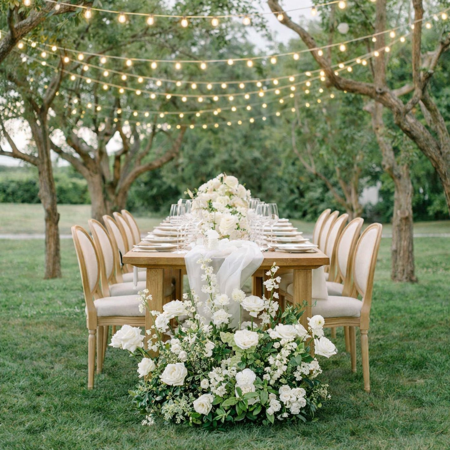 Porcelain Additional Ground Meadow Arrangement styled beside long outdoor banquet table with layered white blooms and romantic garden atmosphere.