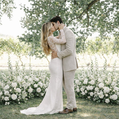 Bride and groom framed by Porcelain Additional Ground Meadow Arrangements featuring soft white blooms and garden-inspired outdoor ceremony styling.