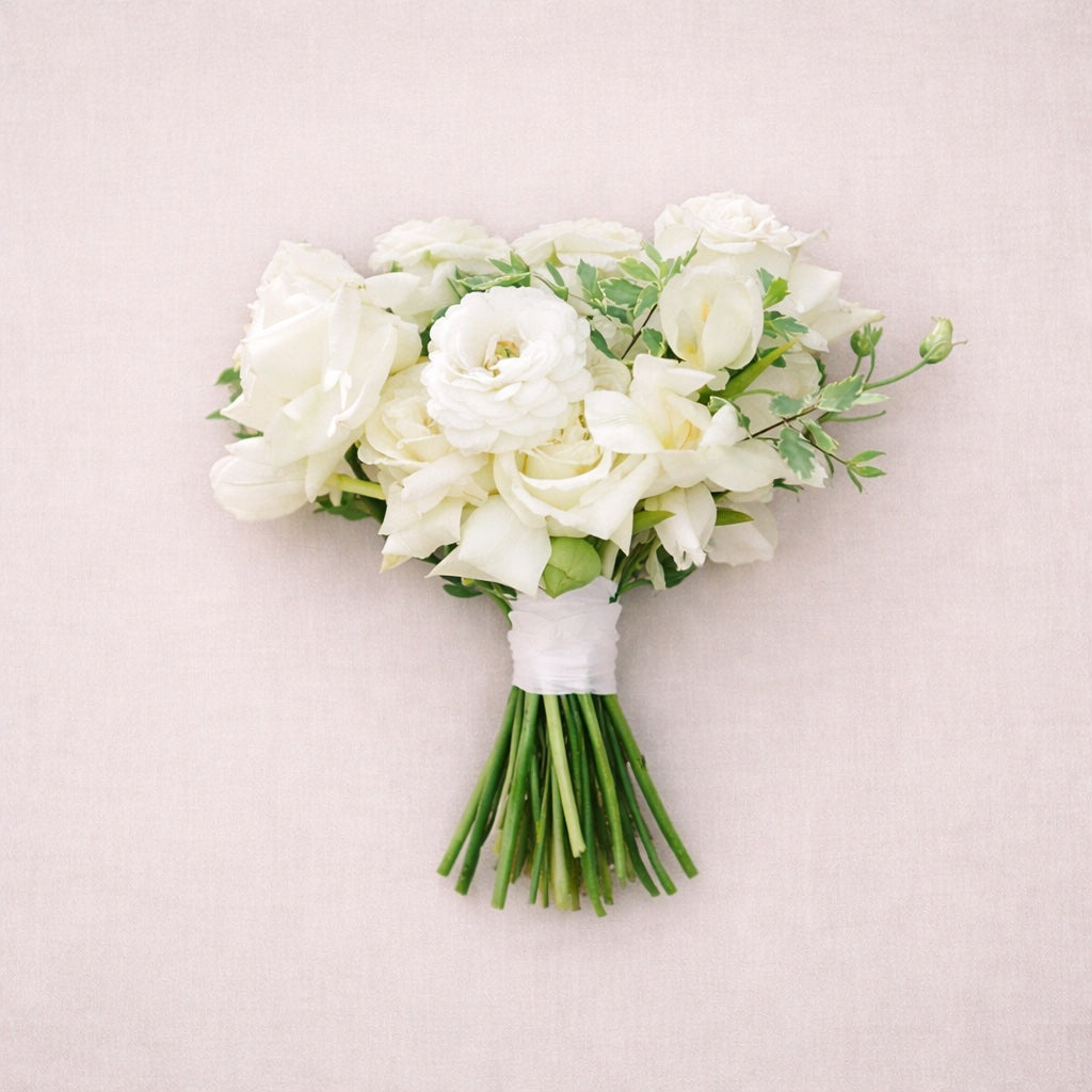 Porcelain bridesmaid bouquet featuring white roses and delicate seasonal blooms styled against soft neutral backdrop.