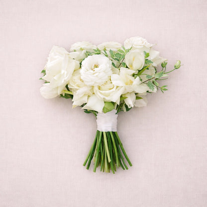 Porcelain bridesmaid bouquet featuring white roses and delicate seasonal blooms styled against soft neutral backdrop.