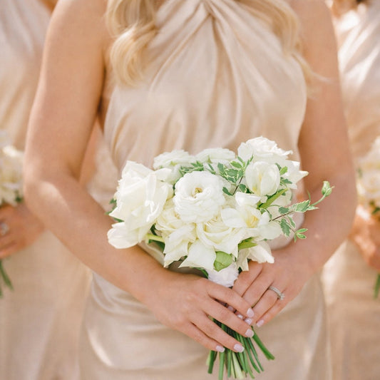Porcelain bridesmaid bouquet with airy white seasonal blooms and soft ivory florals held by bridesmaid in champagne satin dress.