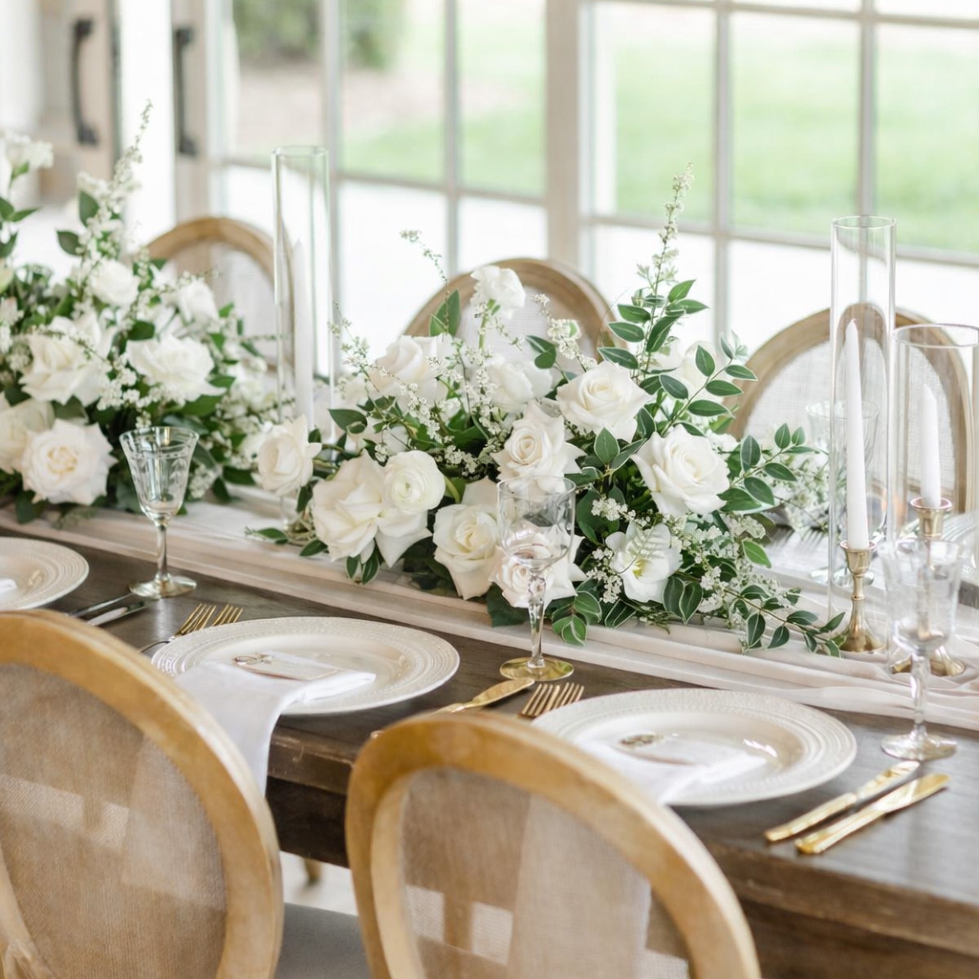 Porcelain Meadow Composition displayed along a long banquet table, featuring airy white flowers and greenery creating a soft, garden-inspired atmosphere.