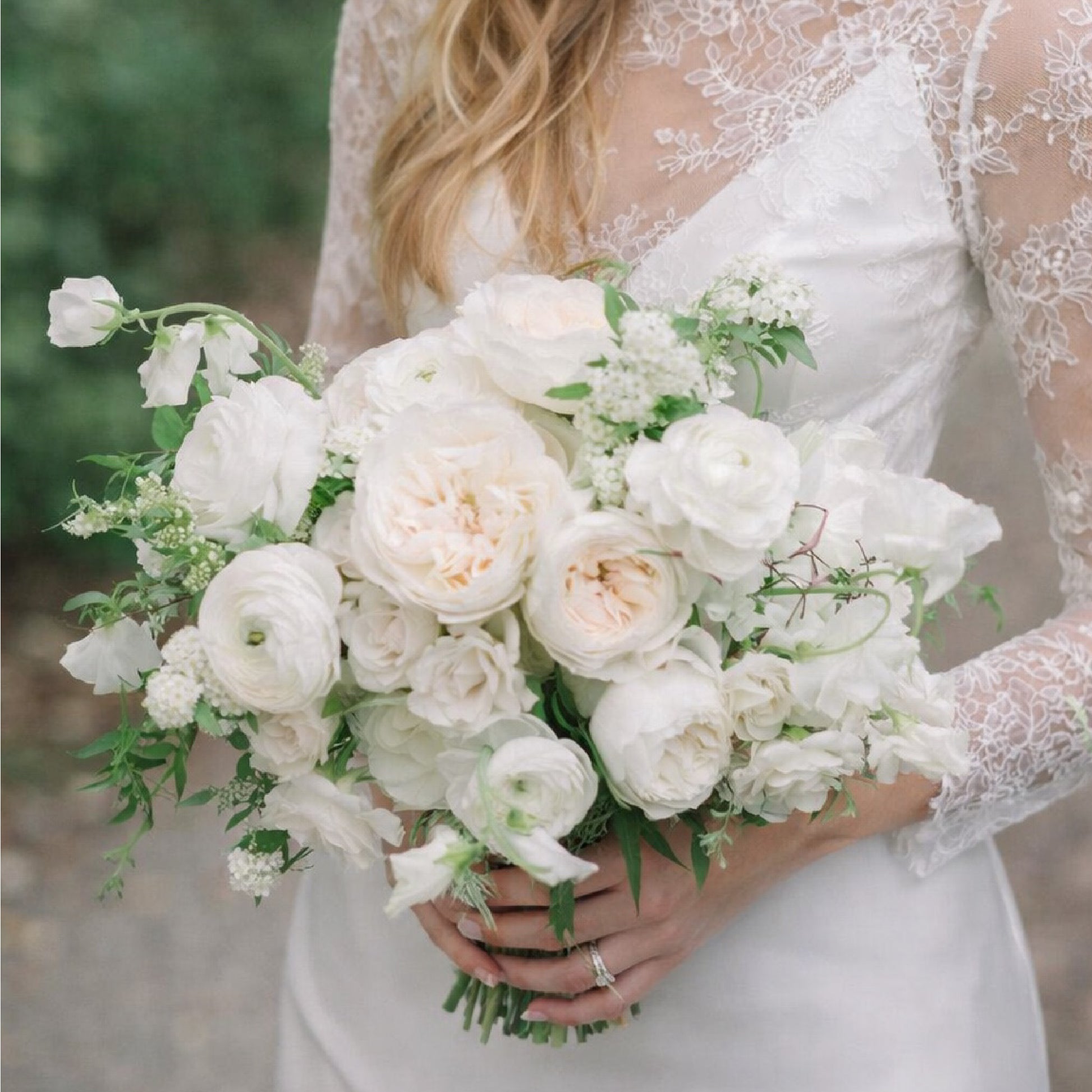 Porcelain bridal bouquet with white garden roses, ranunculus, and airy seasonal blooms held by bride in lace wedding gown.