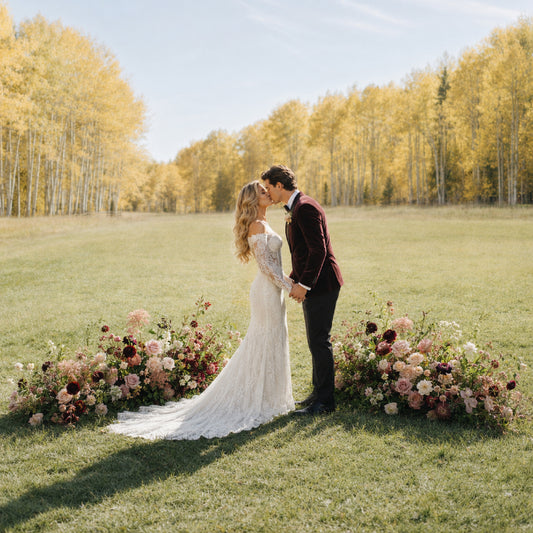 Moody burgundy and blush ground meadow arrangements framing romantic outdoor wedding ceremony