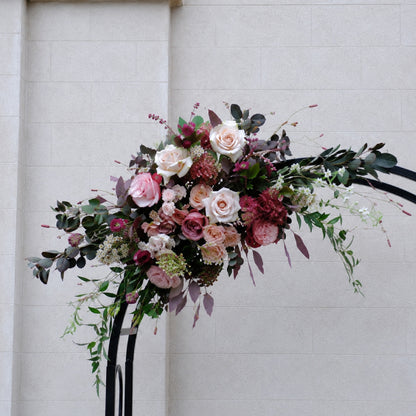 Close-up of large moody burgundy and mauve floral swag for wedding ceremony arch