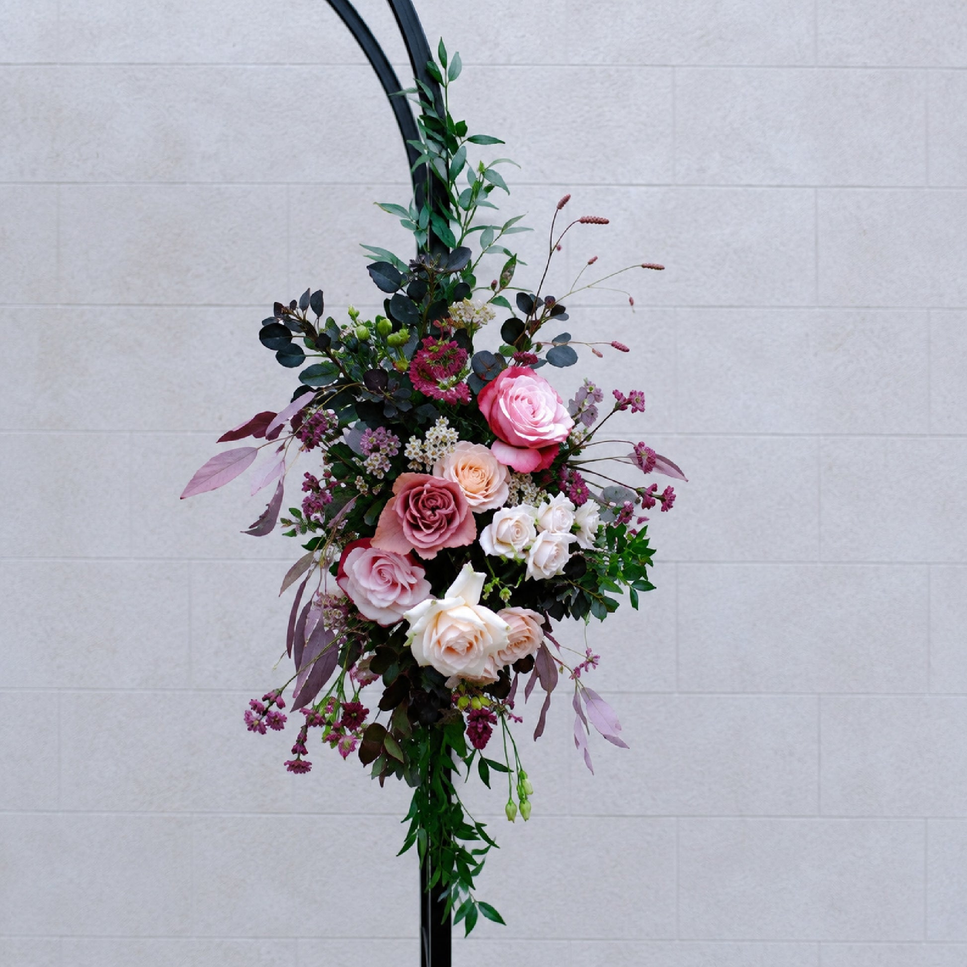 Close-up of small moody burgundy and mauve floral swag for wedding ceremony arch