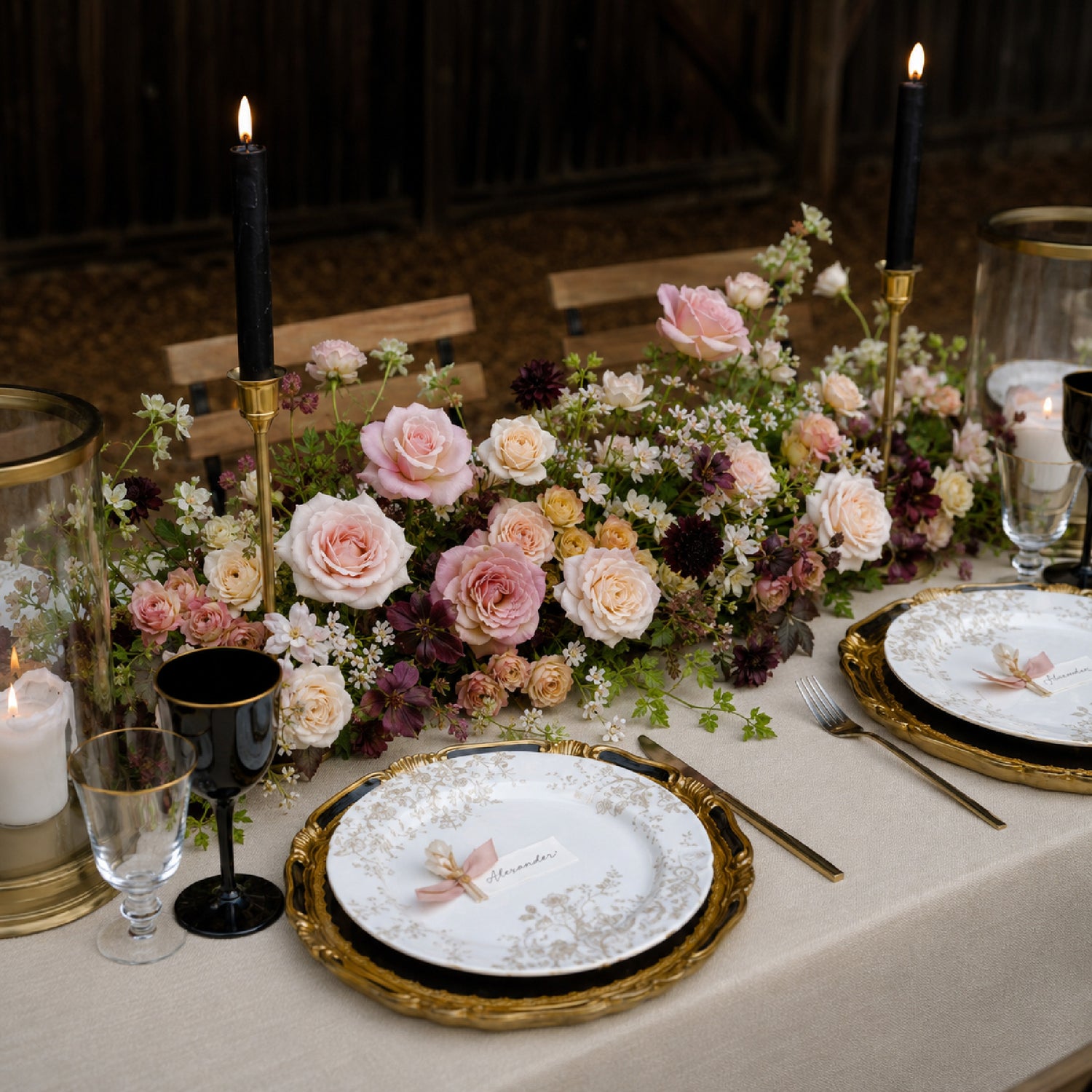 Moody fall wedding floral table runner with burgundy blooms, blush roses, candlelight, vintage plates, and layered tableware by Redolence.