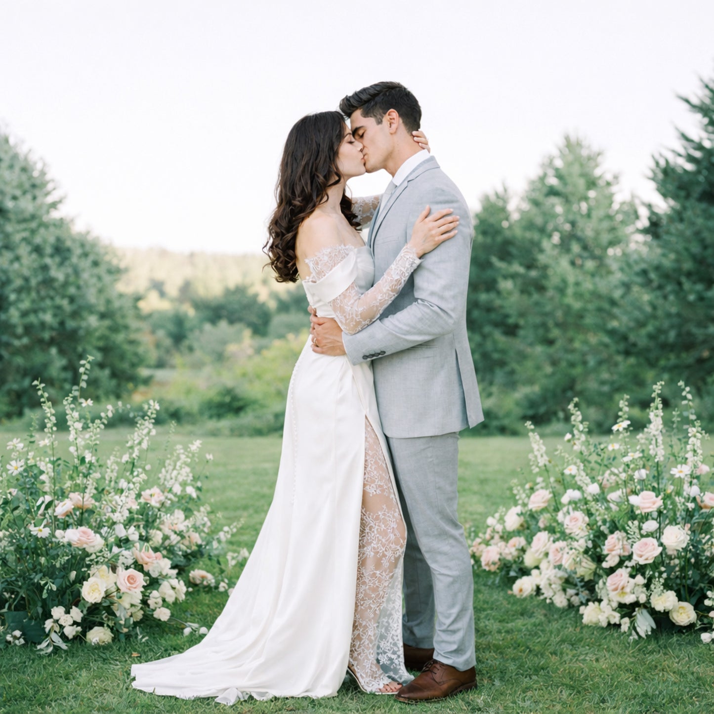 Rosewater ground meadow arrangements with blush and ivory garden blooms framing an outdoor wedding ceremony.