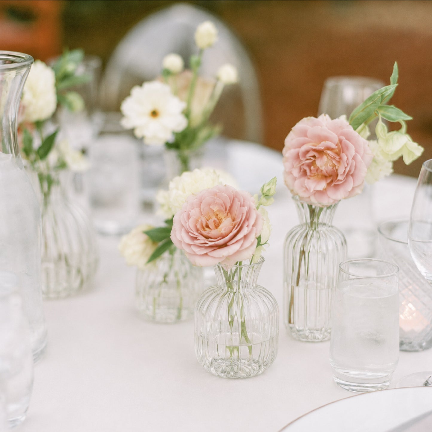 Bud vase trio with blush, cream, and soft neutral flowers styled on romantic reception table.