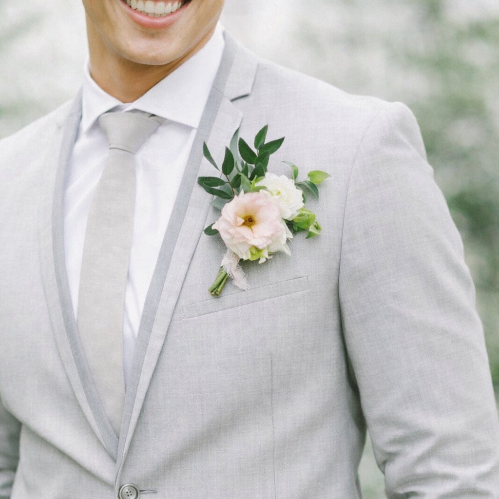 Rosewater boutonnière with blush and ivory blooms pinned to a light grey suit jacket.