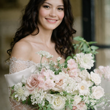 Rosewater bridal bouquet detail with blush roses, cream blooms, airy botanicals, and trailing ribbon in soft romantic palette.