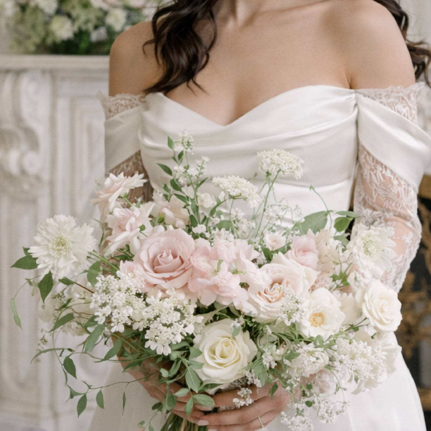 Rosewater bridal bouquet with blush garden roses, ivory seasonal blooms, and airy greenery held by bride in off-shoulder gown.