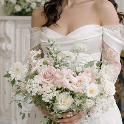 Rosewater bridal bouquet with blush garden roses, ivory seasonal blooms, and airy greenery held by bride in off-shoulder gown.