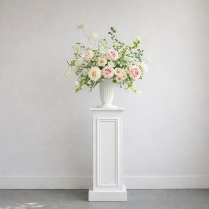 Rosewater ceremony urn arrangement styled on a white pedestal with airy blush and ivory garden florals.