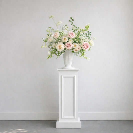 Rosewater ceremony urn arrangement styled on a white pedestal with airy blush and ivory garden florals.