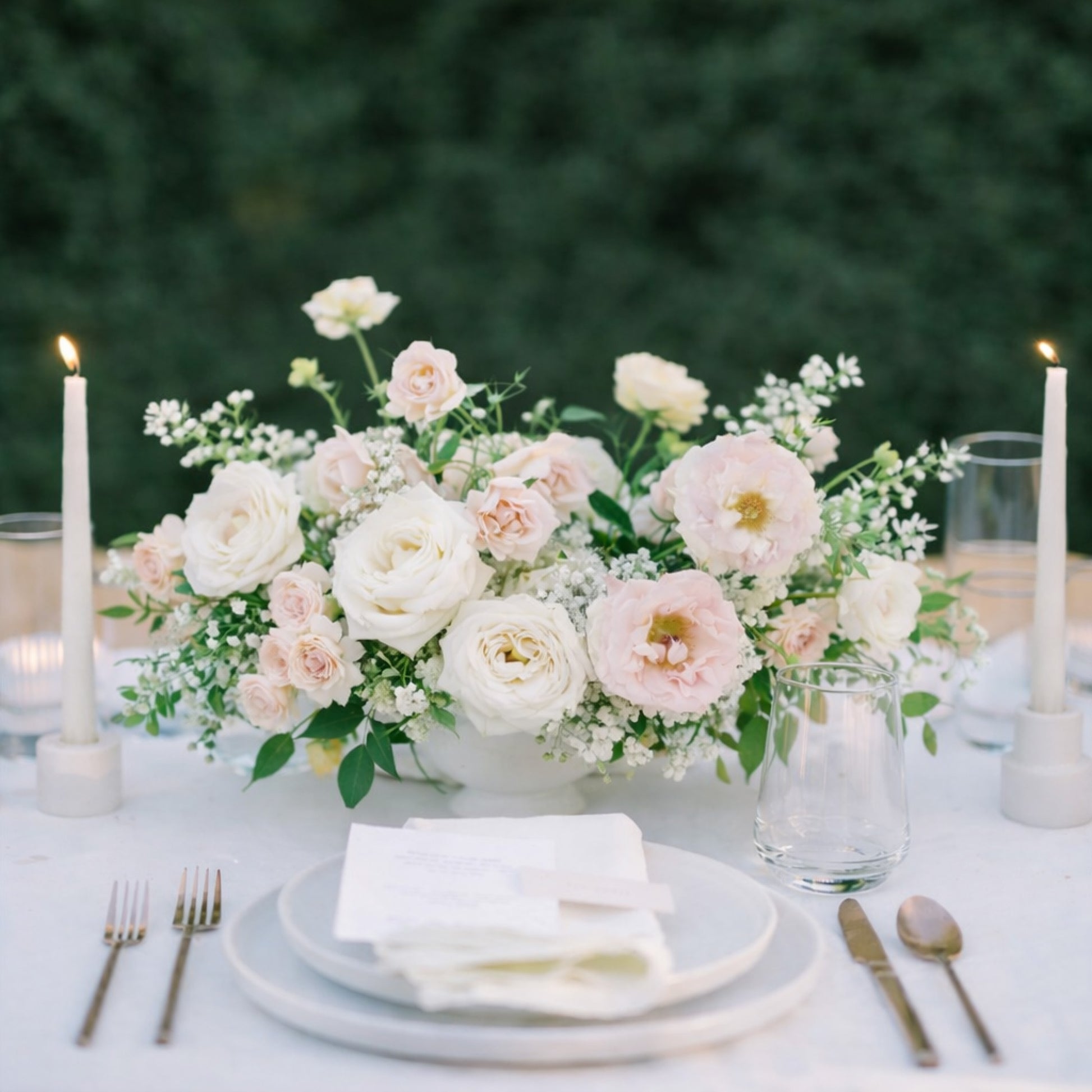 Rosewater large still-life centerpiece with blush and ivory garden blooms arranged in a sculptural ceramic vessel on a candlelit reception table.