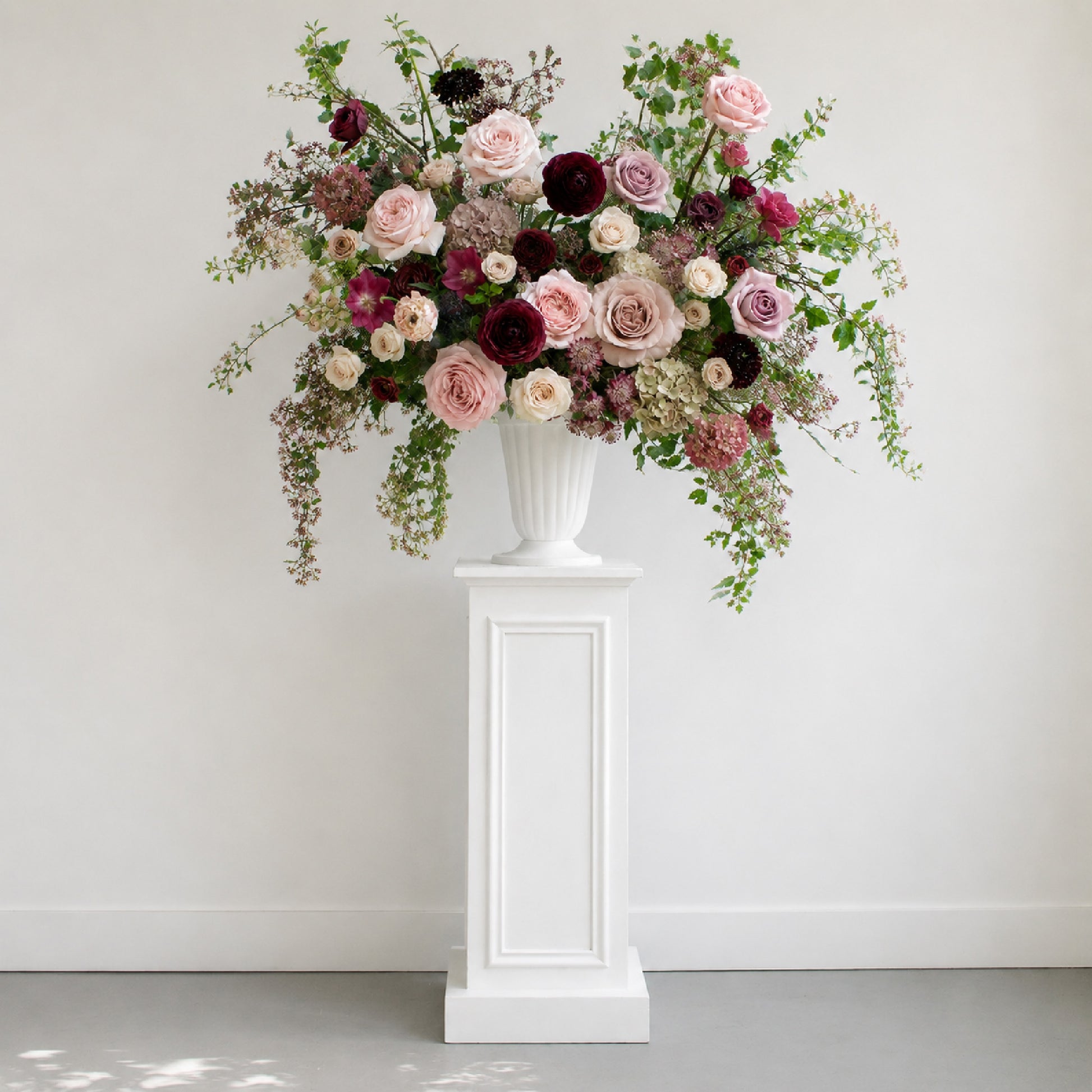 Moody burgundy and mauve ceremony urn flowers displayed on classical pedestal