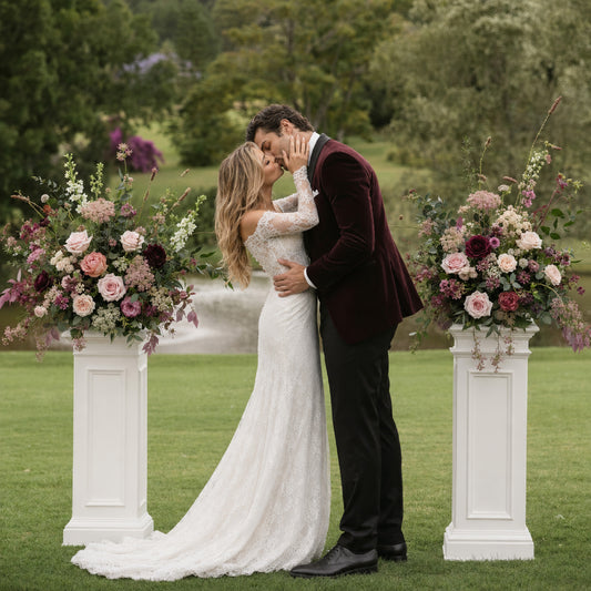 Romantic couple framed by moody meadow flower arrangements on classical columns